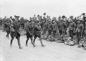 four men dressed in formal military uniform walking on a road flanked by cheering soldiers