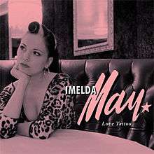 A pink-saturated picture of a woman sitting at a diner table. White text reads "Imelda May Love Tattoo."