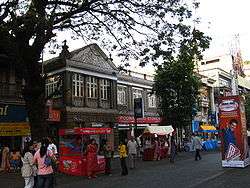 Road shown with a few shops housed in building constructed by the British.