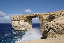 The photograph depicts a rock-filled shoreline, with breaking waves striking at the cliffs.