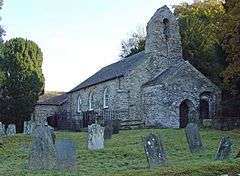 A stone church seen from an angle in a graveyard, with a porch and a bellcote