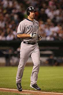 A man in a gray baseball uniform and navy blue batting helmet jogs down a baseline. His jersey reads "New York" in navy blue block print.