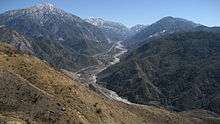 A dry wash threads through a deep evergreen forested canyon between two high gray peaks