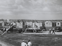 Slightly elevated view of workers constructing an entire neighborhood. The houses are all of similar appearance, with windows and a door.