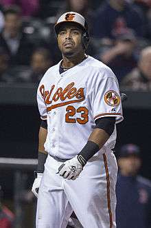 A man wearing a white baseball uniform with "Orioles" and the number 23 written in orange on the chest