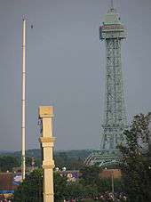 A barely visible figure stands on a tightrope connected by a large pole and a replica of the Eiffel Tower