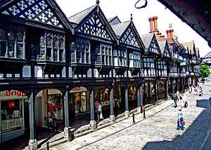 A terrace of shops seen from an angle. The upper storeys are timber-framed with gables; the shops at ground floor level are set back behind an arcade with supporting columns