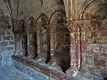 A blind arcade seen from an angle showing four round-headed arches supported on columns with carved capitals; a bench runs along the base