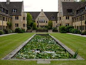A long pool set in a grass lawn; stone buildings of two and three storeys on three sides
