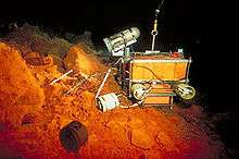 A small box-like robot positioned on orange rocks