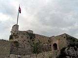 Stone tower with flag left from stone entrance.