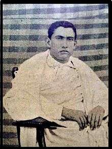 Seated, serious-looking young man dressed in white