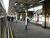 A railway platform with various people walking in different directions on it and a black sign reading "Way out" in yellow letters