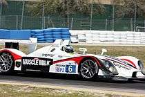 Side view of #6 white sports racing car with the words Muscle Milk on the side