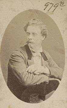 Portrait of Henri with waxed moustache, sitting backwards on a chair, 3/4 to camera, wearing a formal jacket and white bowtie.