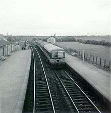 Diesel train entering a station with fields in background