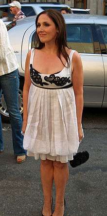 A woman with long brunette hair, wearing a black and white outfit