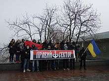 twenty masked activists posing with a Ukrainian flag and a Right Sector banner showing trident as ship anchor at a Euromaidan event in Odessa