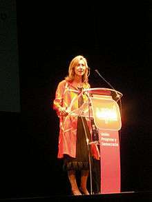 Woman in a dress, speaking at a podium