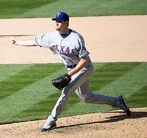 Pitcher in blue cap delivering a sidearm pitch to the plate