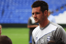 Head and shoulders of young white man with dark spiky hair and wearing a sports shirt