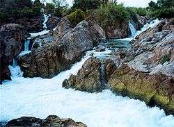 Two mountainous streams flowing across rocks into a pool.