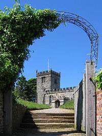 Part of a battlemented church and tower seen through an archway