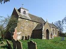 A stone church with a slate roof seen from the southwest, showing the weatherboarded bellcote and the gabled south porch