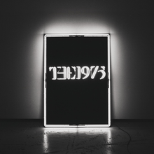 A black-and-white photo showcasing a rectangular, glowing neon sign against a wall in the near-center saying "The 1975".