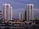 Distant ground-level view of four identical 40-story buildings; each structure has a white concrete facade with balconies at every floor level and a rounded roof.