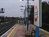 A grey railway station with railway tracks on either side of it, four blue lampposts protruding from the middle of it, and a blue sky above