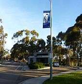 Photo on a light pole of a woman smiling in front of Visitor Information booth, lots of trees