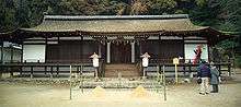 Frontal view of a rather low and wide building with wooden beams and white painted walls.