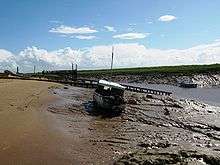 Muddy river bank with a small boat on it. Water can still be seen in the channel to the right.