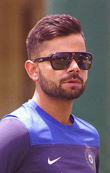 A brown-colored man with a beard, wearing a blue-white shirt.