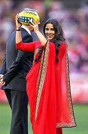 Vidya Balan holds a ball in her hand at a soccer field.