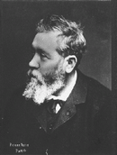 Shoulder-high portrait of man in his sixties with short grey hair and beard wearing a suit