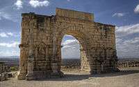 View of a triumphal arch which has two inset columns on each side, in between which are niches, and with a long tablet across the top on which an inscription is written