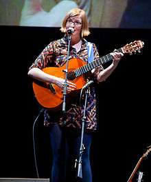 Photograph of Angela playing a guitar and singing into a microphone.