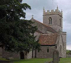 Stone building with square tower partially obscured by tree.