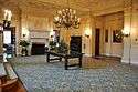 A large carpeted lobby with a center table, fireplace, and chandelier